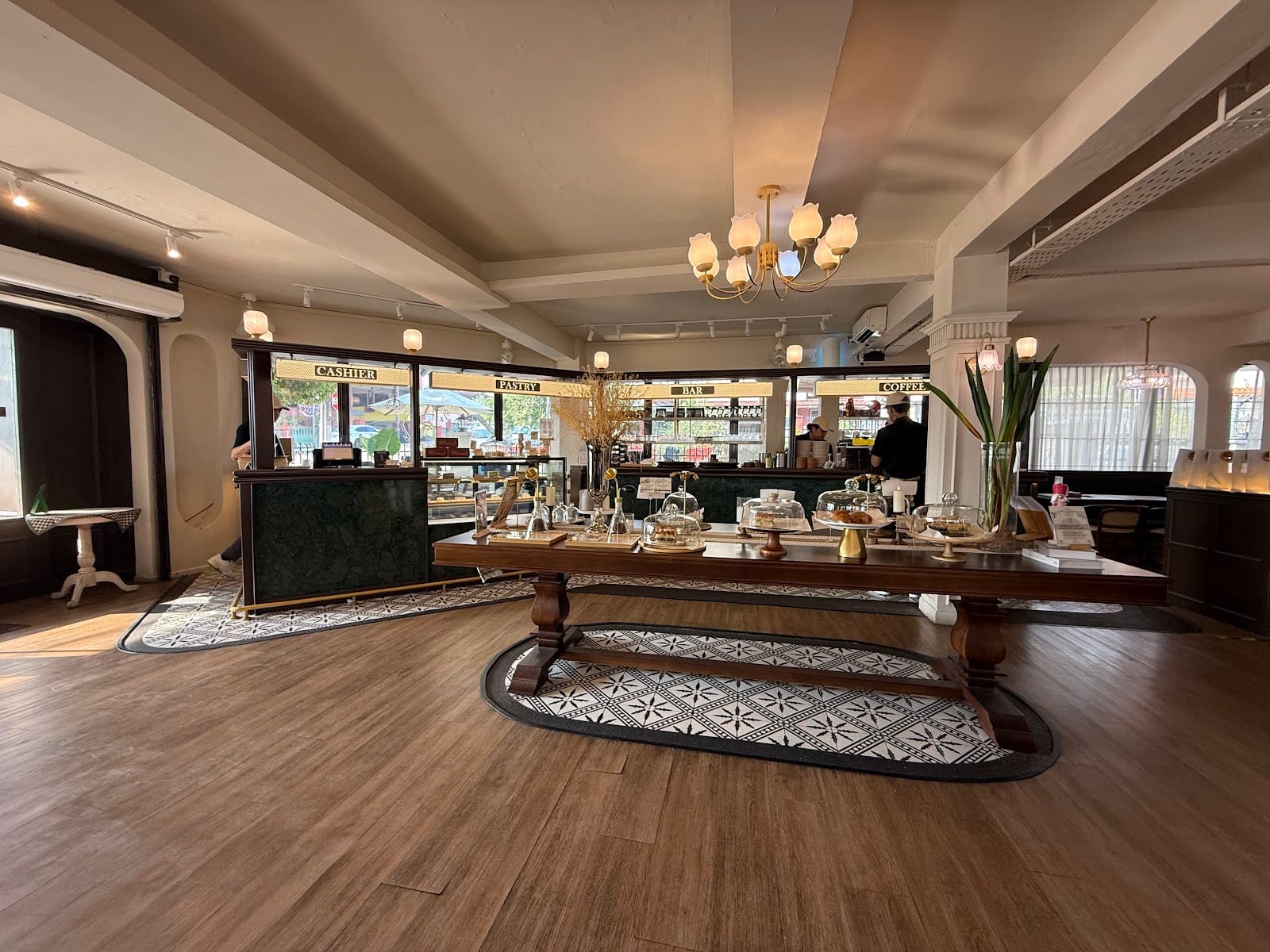 Inside Principle Reserve: a long wooden table under chandeliers, with the pastry and coffee counters behind
