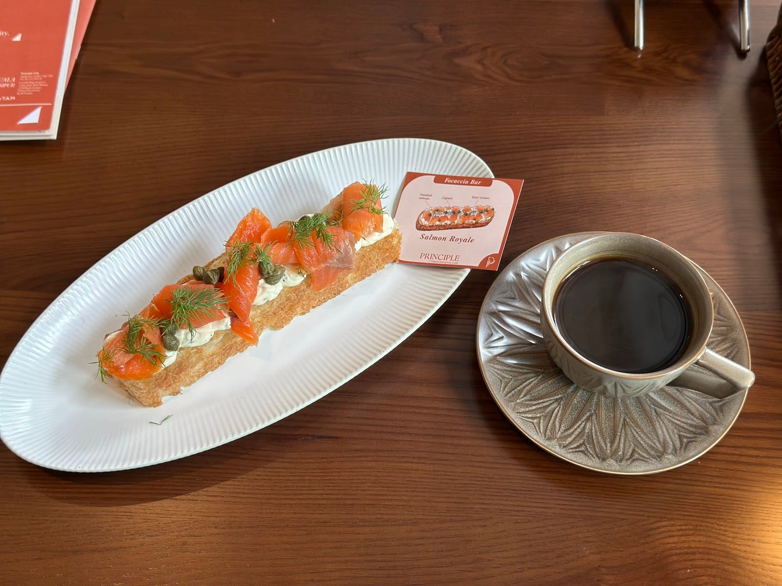 Salmon Royale Focaccia Bar with a black coffee on a wooden table